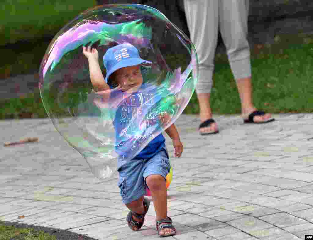 A boy plays with a soap bubble in a Kiev park on a hot day in the Ukrainian capital.