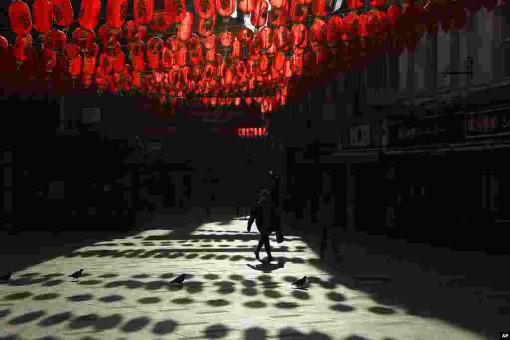 A woman wearing a face mask to curb the spread of coronavirus walks beneath lanterns hung across the street to celebrate the Chinese Lunar New Year which marks the Year of the Ox, in the Chinatown district of central London.