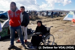 A wheelchair-bound migrant woman waits in the makeshift refugee camp in the Idomeni, Greece, near its border with Macedonia, March 4, 2016. (J. Dettmer for VOA)