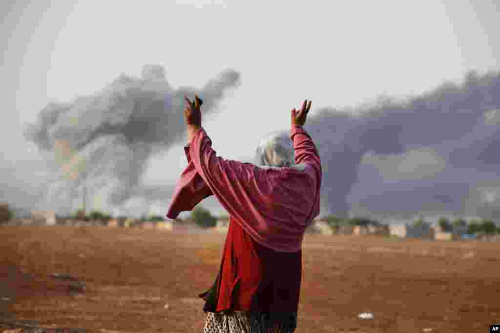 Syrian Kurd Kiymet Ergun, 56, celebrates in Mursitpinar on the outskirts of Suruc, at the Turkey-Syria border, as thick smoke rises following an airstrike by the US-led coalition in Kobani, Syria, Oct. 13, 2014.