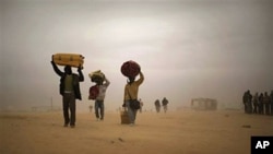Men, who used to work in Libya and fled the unrest in the country, carry their belongings as they walk during a sand storm in a refugee camp at the Tunisia-Libyan border, in Ras Ajdir, Tunisia, March 15, 2011