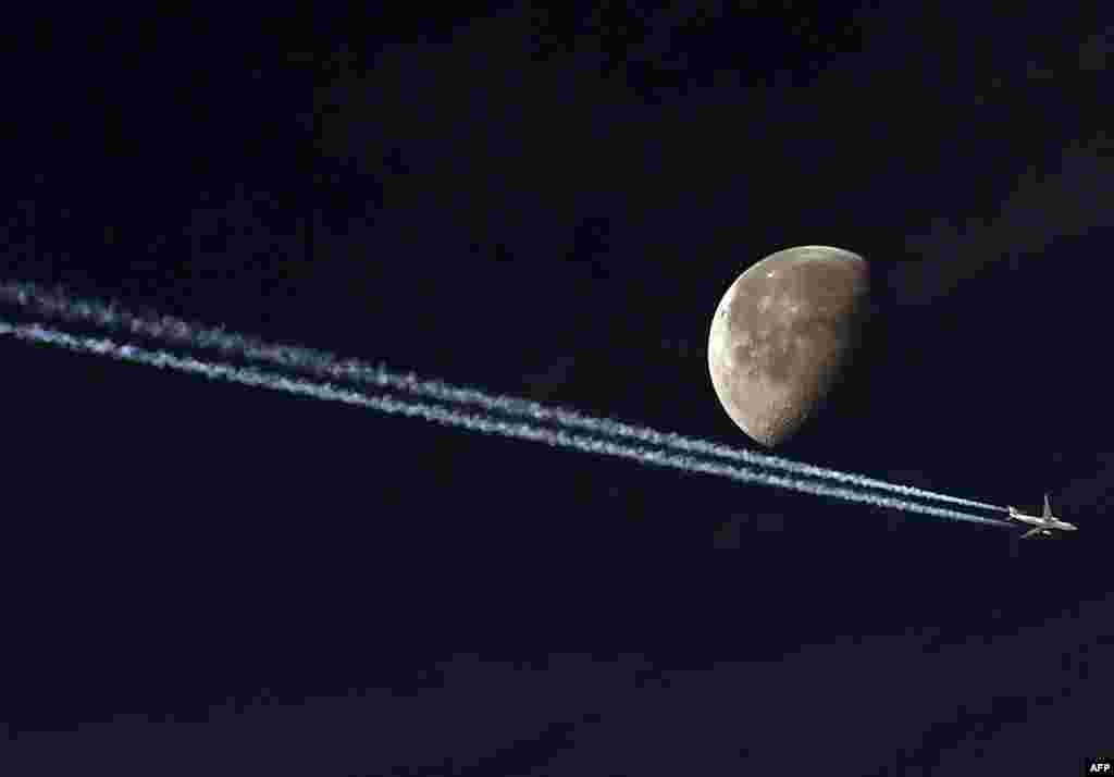 A jetliner leave a vapour trail as it passes in front of the moon in this photo taken from the Algerian capital Algiers.