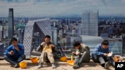 Pekerja konstruksi makan siang dekat sebuah gambar Pusat Distrik Bisnis di luar sebuah lokasi konstruksi di Beijing, China, 6 April 2017. 