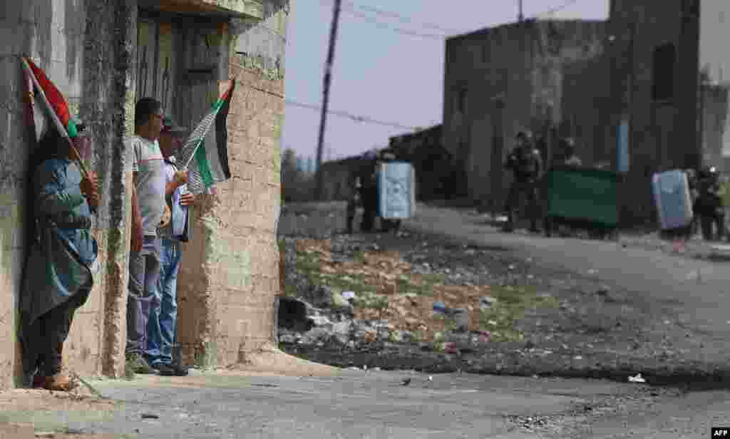 Palestinian demonstrators hide against the wall of a house during clashes with Israeli security forces, following a protest against the expropriation of Palestinian land by Israel, in the occupied West Bank village of Kfar Qaddum near the Jewish settlement of Kedumim.