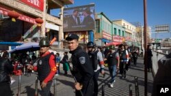 FILE - Armed civilians patrol the area outside the Hotan Bazaar where a screen shows Chinese President Xi Jinping in Hotan in western China's Xinjiang region, Nov. 3, 2017. (AP Photo/Ng Han Guan, File)
