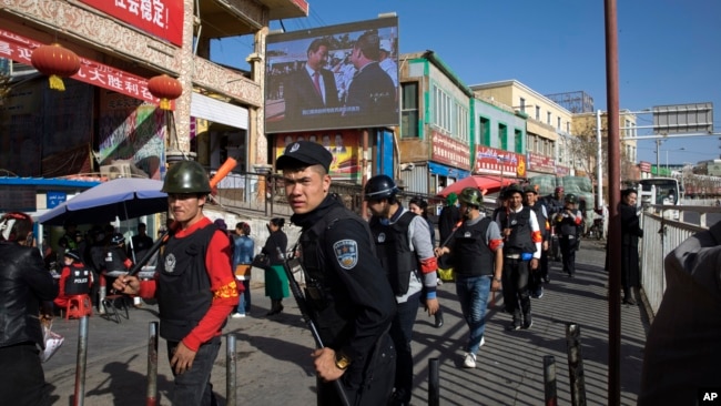 FILE - Armed civilians patrol the area outside the Hotan Bazaar where a screen shows Chinese President Xi Jinping in Hotan in western China's Xinjiang region, Nov. 3, 2017. (AP Photo/Ng Han Guan, File)