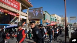 FILE - Armed civilians patrol the area outside the Hotan Bazaar where a screen shows Chinese President Xi Jinping in Hotan in western China's Xinjiang region, Nov. 3, 2017. (AP Photo/Ng Han Guan, File)