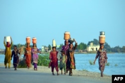 People displaced by flooding in Pakistan carry containers with water near a makeshift camp in Dera Allah Yar town in Jaffarabad district, Balochistan province, on Sept. 2, 2022.