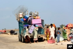 A family carries belongings from a flooded home after heavy rain in Qambar Shahdadkot district of Sindh province, Pakistan, Sep. 2, 2022.