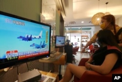 FILE - A customer and a staff member watch a news report on the recent tensions between China and Taiwan, at a beauty salon in Taipei, Taiwan, Aug. 4, 2022.