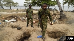 FILE - Nigerian naval personnel walk past deep holes dug by vandals to steal oil from pipelines belonging to the Nigerian National Petroleum Corp. close to Tarkwa Bay, near Lagos' harbor, Jan. 23, 2020.