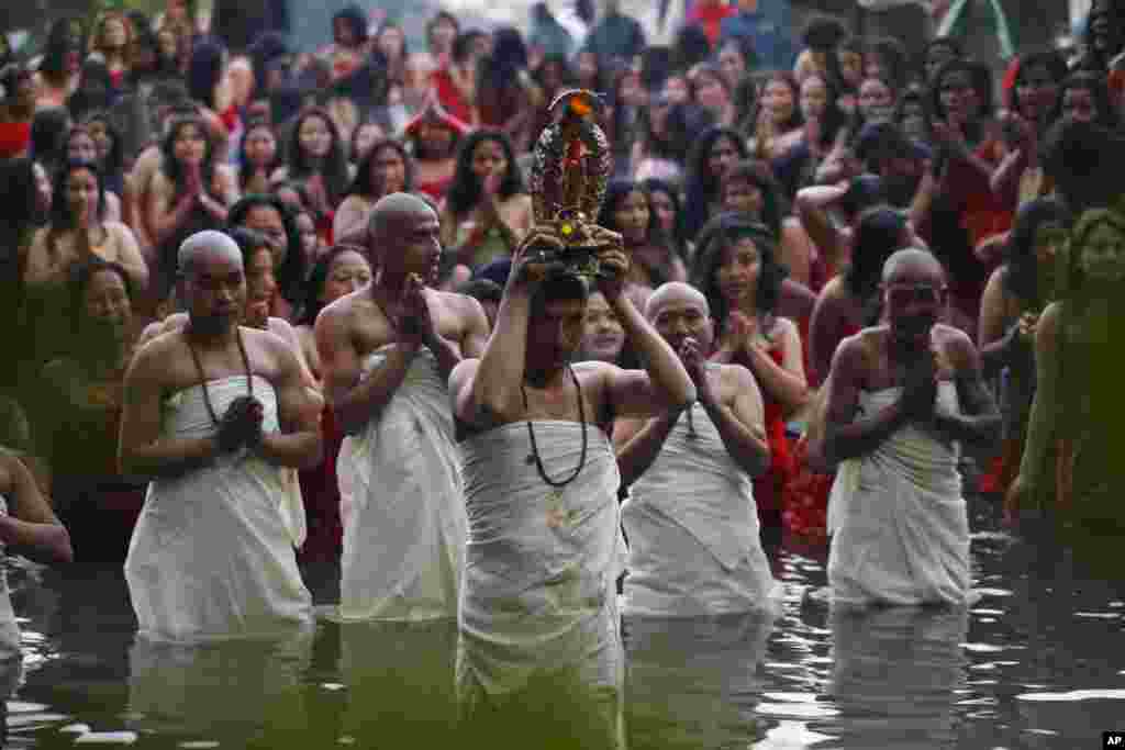 A Nepalese Hindu priest, center, carries the idol of a deity as devotees gets ready to take a holy dip at the Salinadi River on the first day of Madhav Narayan festival, in Sankhu, northeast of Katmandu, Nepal. 