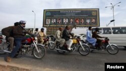 People ride motorcycles past a banner promoting the Eighth D-8 Summit in Islamabad November 21, 2012.