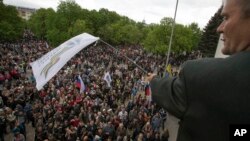 A pro-Russian activist waves a Donbas Republic flag over a crowd celebrating the capture of an administration building in the center of Luhansk, Ukraine, one of the largest cities in Ukraine's troubled east, April 29, 2014, as demonstrators demand greater autonomy for Ukraine's regions.