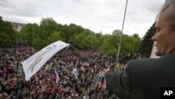 FILE - A Pro-Russian activist waves a Donbas Republic flag over a crowd celebrating the capture of an administration building in the center of Luhansk, Ukraine, one of the largest cities in Ukraine's troubled east, April 29, 2014.