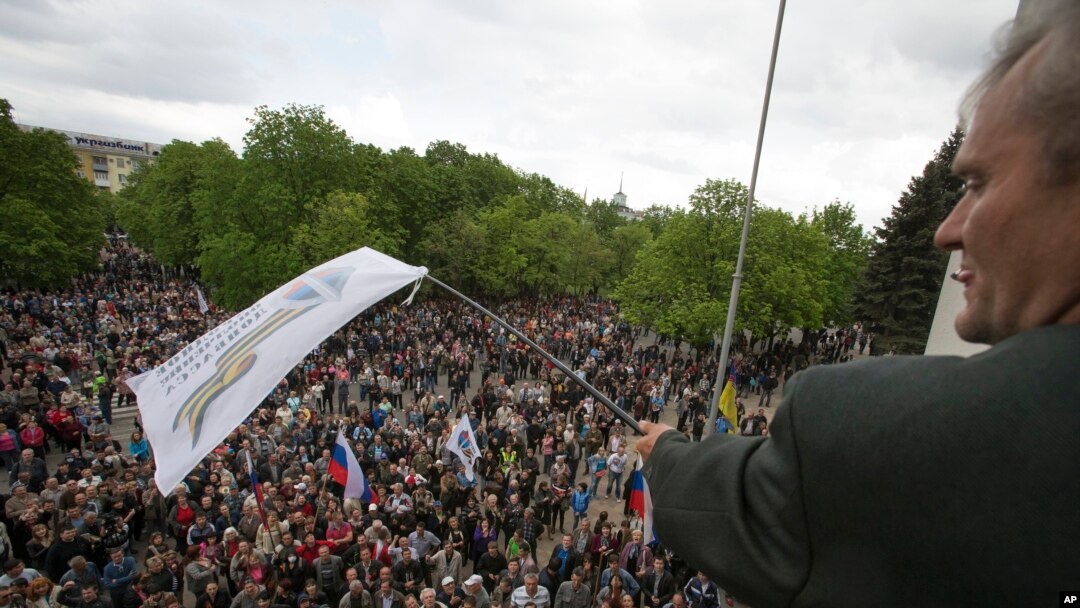 FILE - A Pro-Russian activist waves a Donbas Republic flag over a crowd celebrating the capture of an administration building in the center of Luhansk, Ukraine, one of the largest cities in Ukraine's troubled east, April 29, 2014.