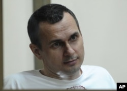 FILE - Oleg Sentsov sits behind glass in a cage at a court room in Rostov-on-Don, Russia, July 21, 2015.