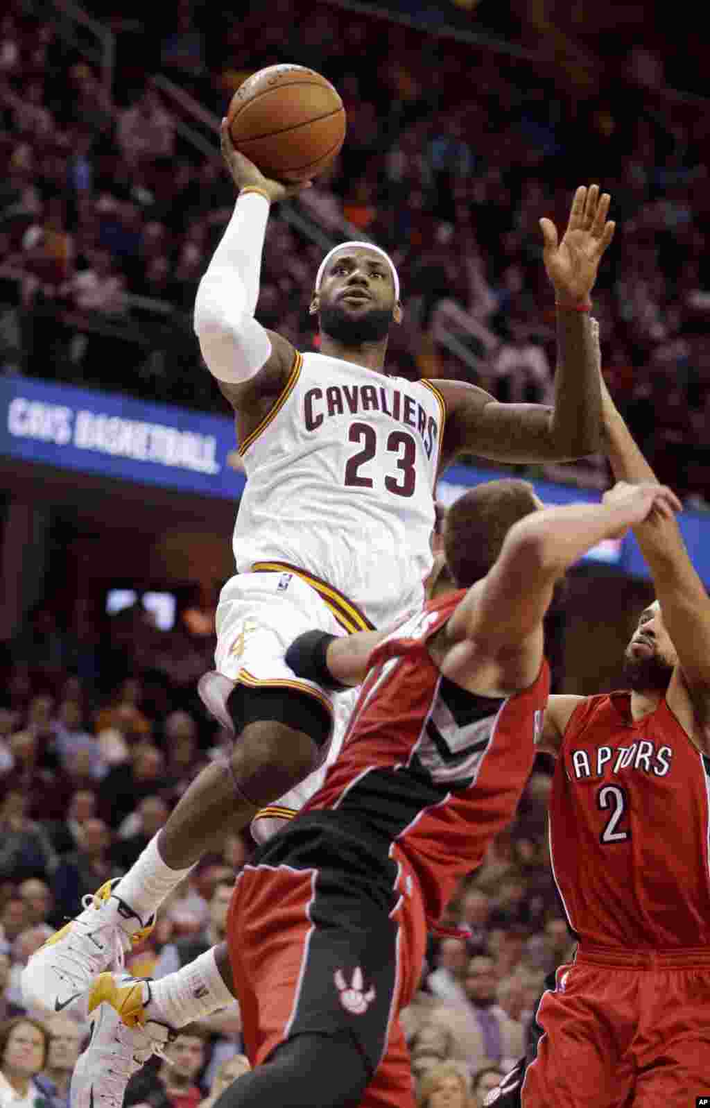 LeBron James (23) joueur des Cavaliers de Cleveland tire face à Landry Fields (2) et Jonas Valanciunas des Raptors de Toronto lors du dernier quart temps du match de NBA du 9 décembre 2014, à Cleveland. James a marqué 35 points pour mener les Cavaliers à la victoire 105-101. &nbsp;