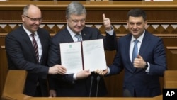 Ukrainian President Petro Poroshenko, center, Prime Minister Volodymyr Groysman, right, and parliament speaker Andriy Parubiy are seen with the newly signed Constitutional amendment on pursuing EU and NATO membership, in Ukraine's parliament in Kyiv, Feb. 19, 2019.