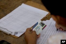 FILE - A member of the ruling United Socialist Party writes takes note of the "fatherland card" of a voter outside a voting center in Valencia, Venezuela, May 20, 2018. Checkpoints known as "red points' are set up outside polling centers to confirm peoples' cards, which are needed to access social programs.