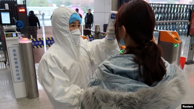 2020年1月24日农历新年前夕，穿着防护服的工作人员检查（到达与武汉北部接壤的）咸宁市乘客的体温。