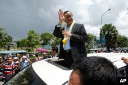 FILE - In this Aug. 16, 2015 file photo, Sam Rainsy, leader of the opposition Cambodia National Rescue Party (CNRP), waves from a car upon his arrival at Phnom Penh International Airport in Phnom Penh, Cambodia as hundreds of cheering supporters greeted him.