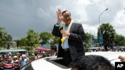 FILE - In this Aug. 16, 2015 file photo, Sam Rainsy, leader of the opposition Cambodia National Rescue Party (CNRP), waves from a car upon his arrival at Phnom Penh International Airport in Phnom Penh, Cambodia as hundreds of cheering supporters greeted him on his return from a trip abroad. The head of Cambodia's opposition party has announced his resignation from the group after the country's long-serving prime minister announced plans for a law that could lead to the party's dissolution. Rainsy announced his resignation Saturday, Feb. 11, 2017 in a letter to his Cambodia National Rescue Party.(AP Photo/Heng Sinith, File)