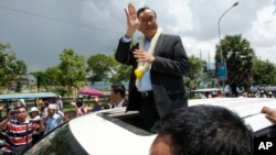 FILE - In this Aug. 16, 2015, file photo, Sam Rainsy, leader of the opposition Cambodia National Rescue Party (CNRP), waves from a car upon his arrival at Phnom Penh International Airport in Phnom Penh, Cambodia as hundreds of cheering supporters greeted him on his return from a trip abroad. The head of Cambodia's opposition party has announced his resignation from the group after the country's long-serving prime minister announced plans for a law that could lead to the party's dissolution. Rainsy announced his resignation Saturday, Feb. 11, 2017, in a letter to his Cambodia National Rescue Party.(AP Photo/Heng Sinith)