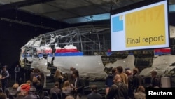 Potongan pesawat MH17 yang telah direkonstruksi sebagian, tampak di latar belakang dalam pengumuman hasil investigasi oleh para pejabat Belanda, hari Selasa (13/10). 