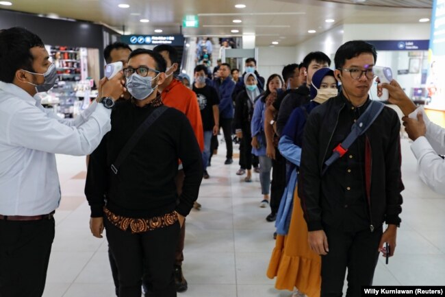 Petugas medis menggunakan termometer untuk mengecek suhu penumpang yang kebanyakan pekerja di stasiun Mass Rapid Transit (MRT), Jakarta, 5 Maret 2020. (Foto: REUTERS/Willy Kurniawan)