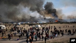 Quelques migrants passent devant une fumée épaisse et des flammes qui s’élèvent du milieu des tentes incendiées dans "la jungle" près de Calais, dans le nord de la France, 26 octobre 2016. 