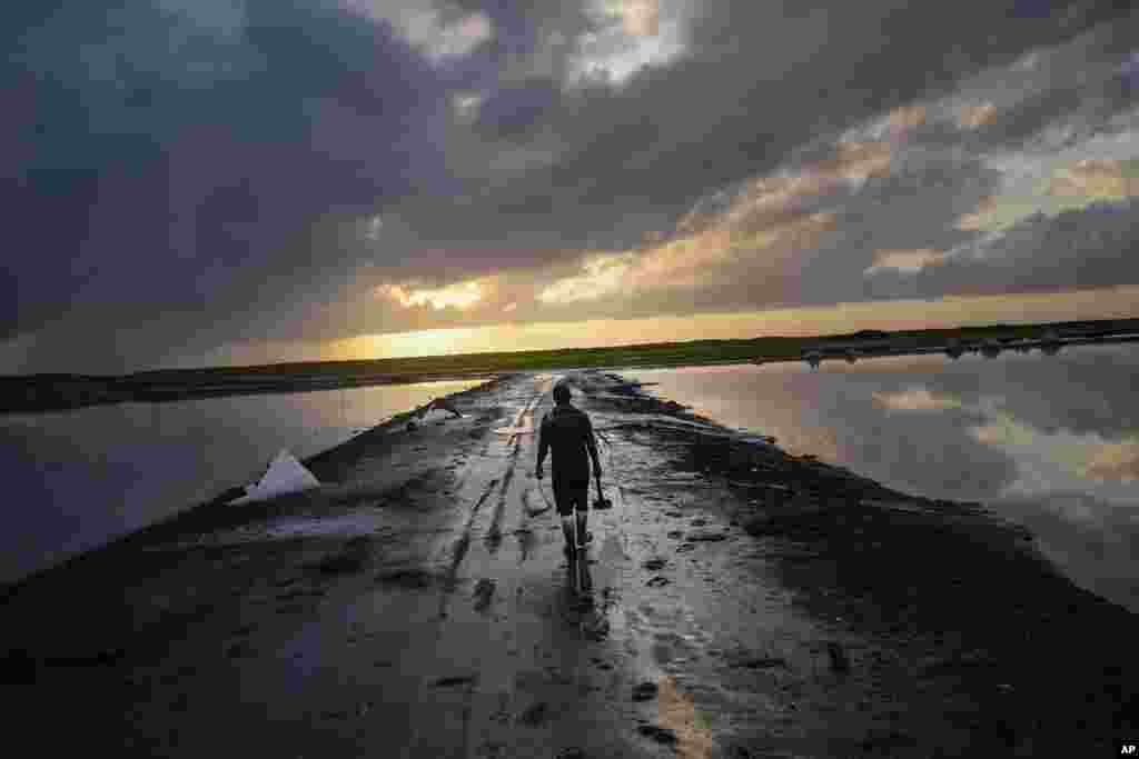 A salt collector carries a shovel and bucket to work the salt flats of Pampatar at sunrise on Margarita Island, Venezuela, Sept. 1, 2022. (AP Photo/Matias Delacroix)