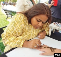 Seniman Henna Kavita Dotia yang datang ke Amerika Serikat dari India, melukis desain daun yang rumit di tangan orang-orang.  (Blok Deborah/Suara Amerika)