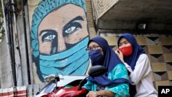 Dua perempuan mengenakan masker sambil naik motor di Jakarta, Indonesia (dok: AP/Dita Alangkara)