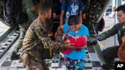 A US Marine helps typhoon survivors as they arrive at Villamor airbase from the Philippine city of Tacloban.