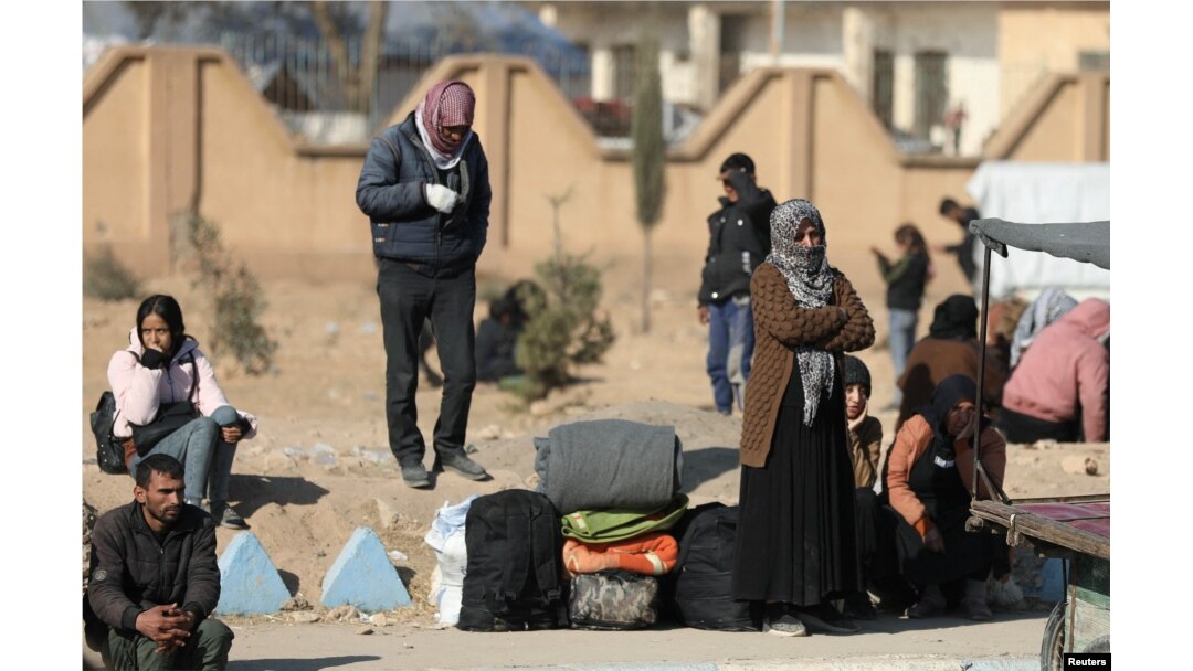 A displaced woman who fled the Aleppo countryside stands near belongings in Tabqa, Syria, Dec. 4, 2024.