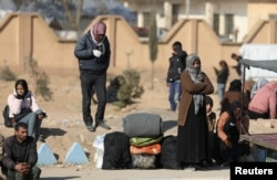 A displaced woman who fled the Aleppo countryside stands near belongings in Tabqa, Syria, Dec. 4, 2024.