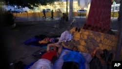 Un pequeño grupo de migrantes que esperan para solicitar asilo duermen en la entrada del puente internacional Puerta de México en Matamoros, en el estado mexicano de Tamaulipas, el viernes 28 de junio de 2019. (AP Foto/Rebecca Blackwell)