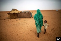 FILE - In this photo released by the United Nations African Union Mission in Darfur (UNAMID), a woman holds hands with her daughter as they walk at the Zam Zam refugee camp for internally displaced people (IDP) in North Darfur, Sudan.