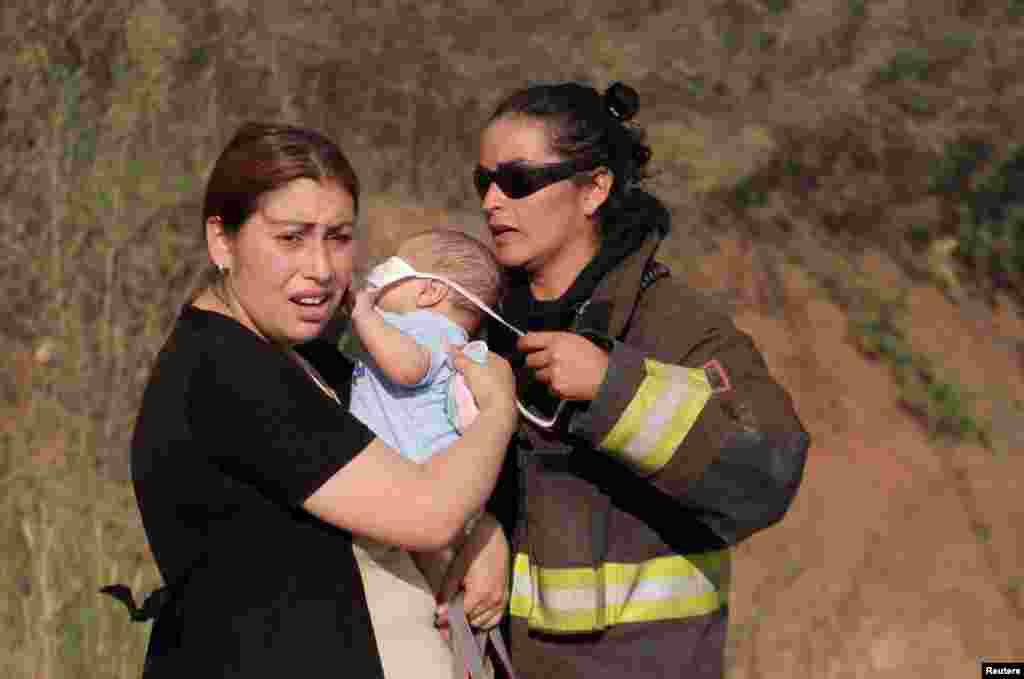 A firefighter covers a baby with a mask during a forest fire in the town of Penco in the Concepcion region, south of Chile, Jan. 25, 2017.