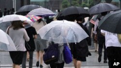FILE - Pedestrians cross a road in the wind and rain as Typhoon Shanshan approaches, Aug. 8, 2018, in Tokyo. Western Japan is bracing for Typhoon Cimaron, which could bring 800 mm (32 inches) of rain to Shikoku.