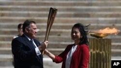 Hellenic Olympic Committee President Spyros Capralos, left, gives the Olympic torch to the former Japanese swimmer Imoto Naoko during the Olympic flame handover ceremony for the 2020 Tokyo Summer Olympics, in Athens, March 19, 2020. 