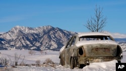 Snow covers the burned remains of a car after wildfires ravaged the area Sunday, Jan. 2, 2022, in Superior, Colo.