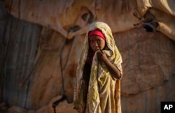 A young Somali girl stands outside her makeshift hut at a camp of people displaced from their homes elsewhere in the country by the drought, shortly after dawn in Qardho, Somalia, March 9, 2017.