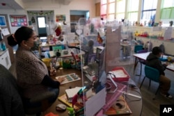 FILE - Surrounded by protective shields, a pre-kindergarten teacher instructs her class at West Orange Elementary School in Orange, California, March 18, 2021.