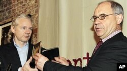 Former Swiss banker Rudolf Elmer hands two CD cases full of files to WikiLeaks founder Julian Assange, left, following a news conference at the Frontline Club in London, 17 Jan 2011