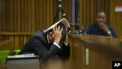 Oscar Pistorius covers his head with his hands and a notebook as he listens to forensic evidence during his trial in court in Pretoria, March 13, 2014. 