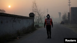 Artist Liu Bolin wearing a vest with 24 mobile phones walks in smog as he live broadcasts air pollution in the city on the fourth day after a red alert was issued for heavy air pollution in Beijing, China, Dec. 19, 2016.