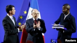 Le Premier ministre français Manuel Valls et ministre de l'Intérieur Bernard Cazeneuve applaudissent comme Lassana Bathily, 24, détient ses papiers de citoyenneté lors d'une cérémonie au ministère de l'Intérieur à Paris, 20 janvier 2015.