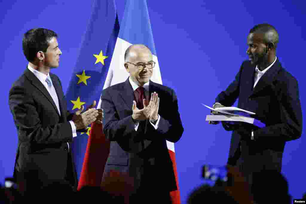 French Prime Minister Manuel Valls and Interior Minister Bernard Cazeneuve applaud as Lassana Bathily, 24, holds his citizenship papers during a ceremony at the Interior Ministry in Paris, Jan. 20, 2015.